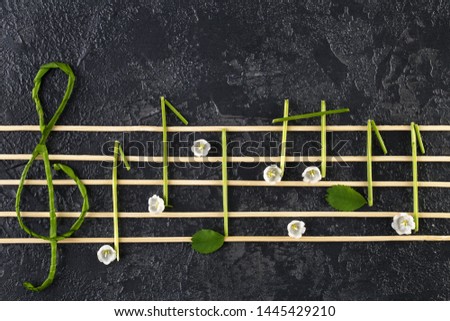 Musical notes conception. Wooden musical notes and flowers. Creative music notes made of flowers on dark background. Top view, Flat lay