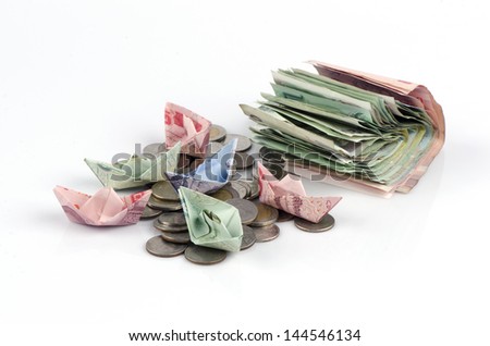 Thai money folded into the shape of a boat and coins isolated over white