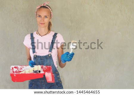 Beautiful woman with a brush and roller for painting. Background gray cement wall.