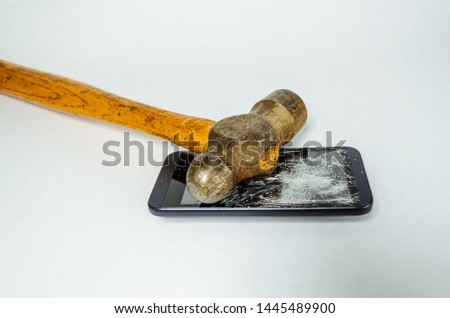 Hammer laying on top of a shattered cell phone laying horizontally on a white background