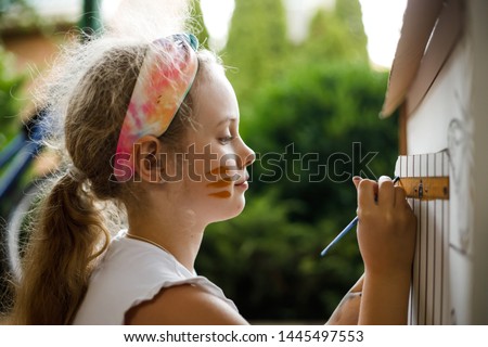 Girl paints a cardboard house at summer day, outdoor