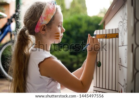 Girl paints a cardboard house at summer day, outdoor