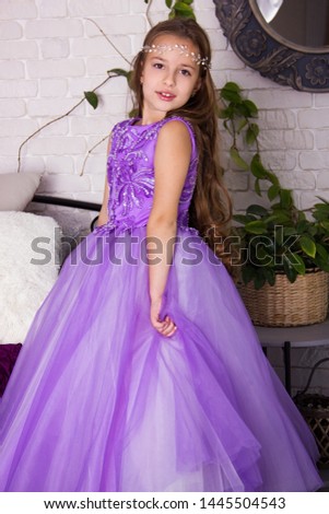 little girl in violet shiny dress with bow. kid christmas costume. young girl princess in white room is standing in violet fancy skirt