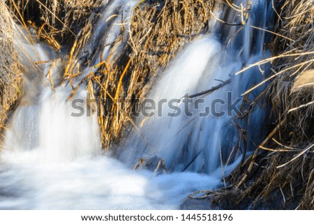 Long-awaited spring creeks flow over ravines and hills on a sunny day. Water rapids and waterfalls of streams among the dry grass. Beautiful spring landscape.