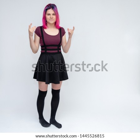 Full-length portrait of young pretty teenager girl in burgundy T-shirt and black dress with beautiful purple hair on a white background in the studio. Talking, smiling, showing hands with emotions.