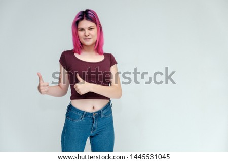 Full-length portrait of a young pretty teenager girl in jeans and a vest with beautiful purple hair on a white background in the studio. Talking, smiling, showing hands with emotions.