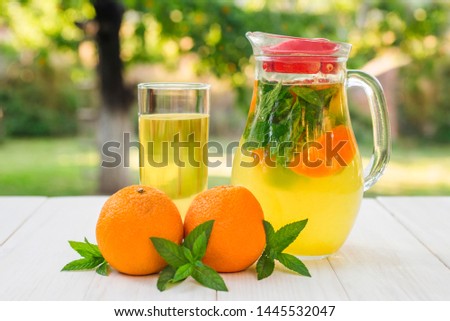 Lemonade pitcher with orange, mint and ice on garden table. Homemade orange lemonade with mint.