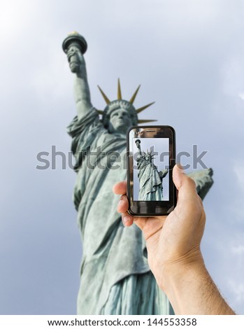 tourist takes a picture with his mobile of statue of liberty in new york