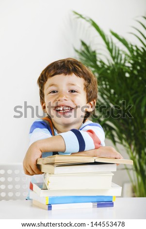 Little boy with a books looking at camera./ Smiling schoolboy studying in home.