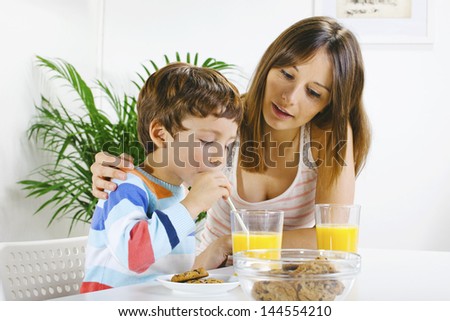 Little boy eating cookies and drinking orange juice with her mum./ Mother and son having breakfast.