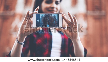 Selective focus on woman's hands holding modern mobile phone and making selfie for updating profile picture in social network.Image of young female taking picture on cellular camera during strolling