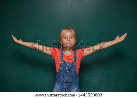 Back to school concept. School child (girl) in classroom. Funny kid against green chalkboard.. Idea and creativity concept. Copyspace on chalkboard background