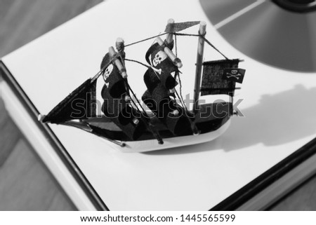 A tiny toy pirate ship on a wooden table top. This image can also be used to represent piracy or copyright infringement. 