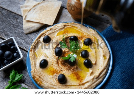 Traditional hummus plate with black olives and paprika on wooden background