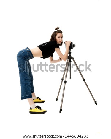 Beautiful brunette girl in a jacket and jeans on a white background at the tripod with an old vintage movie camera