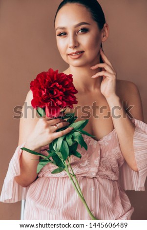 A young woman with a bunch of peonies posing for a camera in the studio