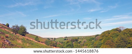 a long panoramic view of west yorkshire countryside with fields and moors above the woodland in hardcastle crags with a blue sunlit cloud sky