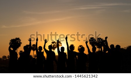 The silhouette of a group of people is raising his hand, pointing up, showing the morning victory against the sugar palm in the Thai countryside.