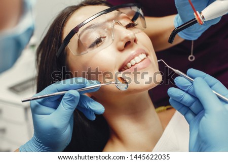 The dentist treats the girl's teeth. A young woman visited a dentist. The doctor works with an assistant