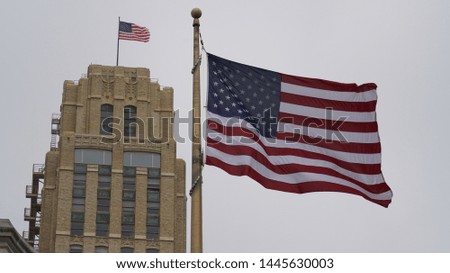 Two US Flags waving up in the air. American Flag close-up with another American Flag on the background, on top a skyscraper