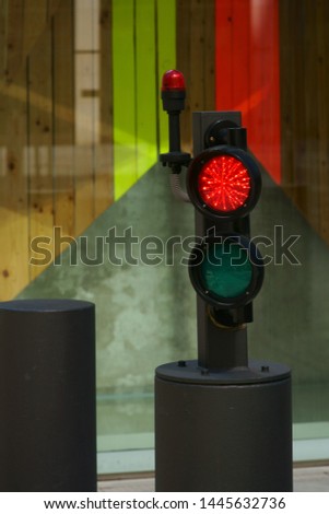 A bollard with a light barrier and traffic light on the driveway to a skyscraper.