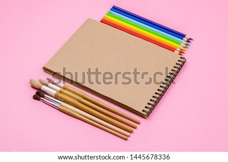 Watercolour brushes, Coloured pencils, notebook isolated on pink background for mockup. Flat lay, top view. Back to school concept.