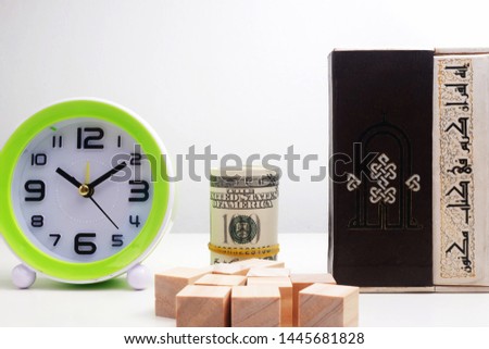 A picture of clock, money, wooden block and Qoran. It is islamic concept picture. The translation for arab word is the word in Qoran is truth and not been authored.
