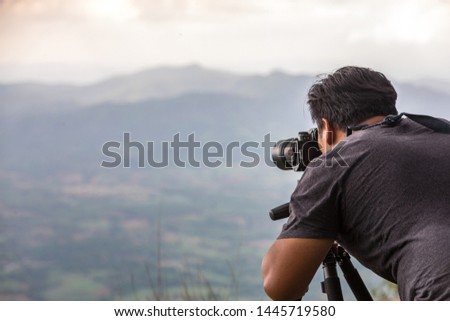 Cameraman photographer travel take a photo with tripod at cliff precipice on mountain he take to layer of mountain and small village, selective focus.