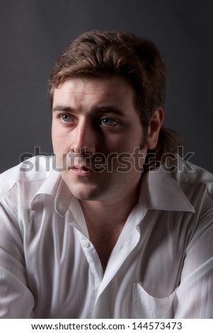 Handsome man posing in white shirt on dark background in studio.