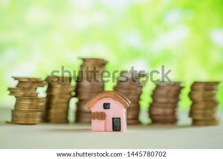 Investment property concept. Mini house and stack of coins with green blur background. 
