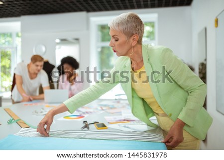 Working process. Elderly woman fashion designer working in a studio using a measuring tape