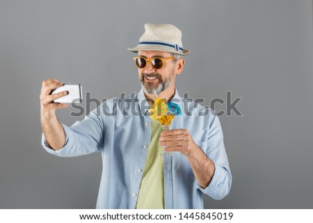 portrait of middle aged man summer dressed drinking cocktail and using cellphone on gray background
