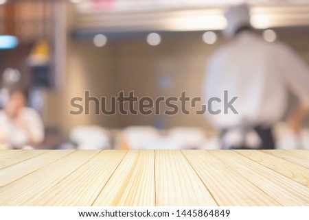 Empty wood table top with Chef cooking in restaurant kitchen abstract blurred defocused background