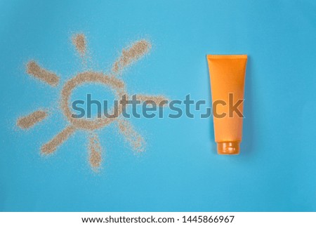 Sun drawn by the sand on blue background. Sunscreen on blue background. Top view.