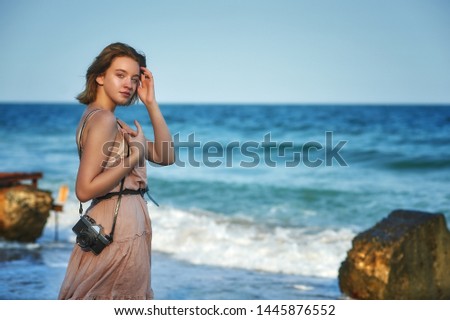 Young tourist girl with a camera on the coast. A girl in a light summer dress . The concept of active recreation