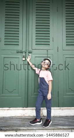 Asian child girls wear denim bib and fashion post caps on the front of the old green door.