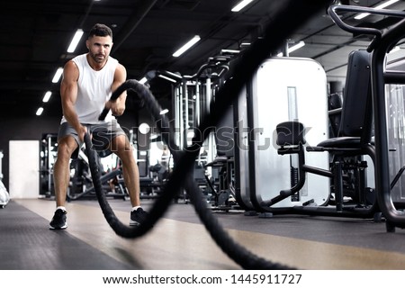 Athletic young man with battle rope doing exercise in functional training fitness gym. Royalty-Free Stock Photo #1445911727