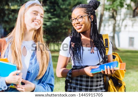 Image of a two happy emotional young pretty multiethnic friends women students walking talking laughing outdoor in university campus park in sunny morning. Different races women friendship concept.