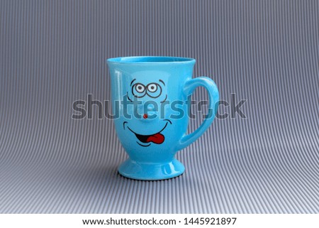 Blue mug of coffee with happy smile face on gray background. Good morning, creative greeting card concept