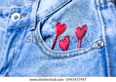 Blue jeans and red hearts from pocket on black background top view flat lay. Detail of nice blue jeans. Jeans texture or denim background. Trend clothing. Fashion, Love to jeans. Selective focus