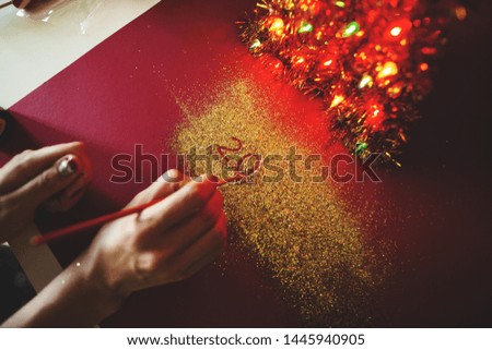 The woman's hand paint the figure of 2020 in the claret background with sparkles. New Year's concept