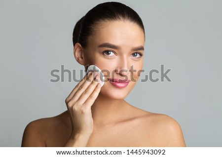 Woman Cleaning Face With Cotton Pad Over Grey Studio Background