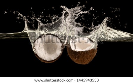 Big tropical splash. Ripe coconut halves falling into water, black background