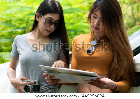 Attractive young asian women tourist with map in hands is in search of new adventures. Natural background sunlight, daylight and tree. tourist vacation concept