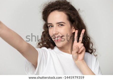 Girl hold webcam raised hand font view showing fingers symbolic devil horns rock and roll gesture posing isolated on grey head shot studio background, using smartphone takes self portrait record video