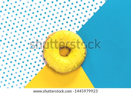 One tasty fresh Donut with yellow glaze on matching yellow and blue and polka dot color block background. Top view flat lay with copy space