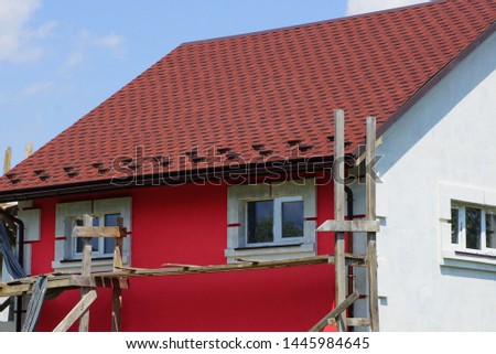 part of an unfinished house with a red wall and windows under a brown tiled roof