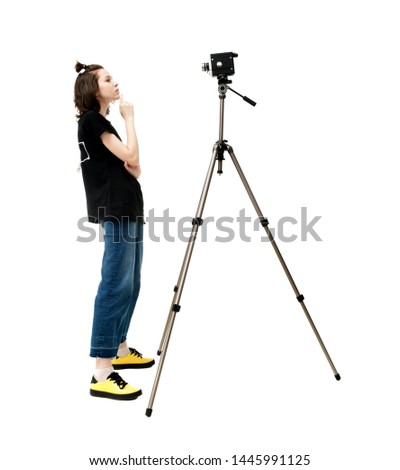 Beautiful brunette girl in a jacket and jeans on a white background posing in front of an old vintage movie camera mounted on a tripod, in isolation