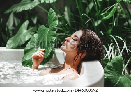 Woman relaxing in round outdoor bath with tropical flowers, organic skin care, luxury spa hotel, lifestyle photo Royalty-Free Stock Photo #1446000692