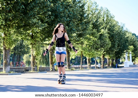 Young pretty brunette woman, riding roller blades in city park in the morning. Fit sporty girl, wearing black top and white shorts, roller skating in action. Full-length portrait of slim sportswoman,